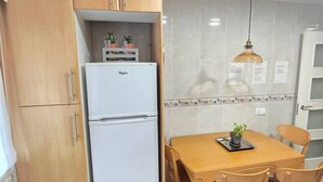 Una cucina compatta con frigorifero bianco, mobili in legno, zoccolo in piastrelle e tavolo con sedie.