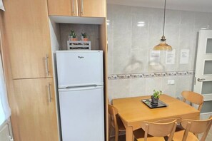 Cocina compacta con refrigerador blanco, gabinetes de madera, salpicadero de azulejos y una mesa de comedor con sillas.
