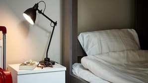 Una cama bien hecha con ropa blanca, una mesita de noche con una lámpara y una maleta roja.