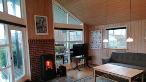 Ein gemütliches Wohnzimmer mit Kamin, Fernseher, Sofa und großen Fenstern.