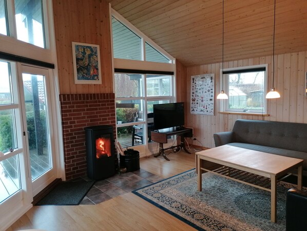 Ein gemütliches Wohnzimmer mit Kamin, Fernseher, Sofa und großen Fenstern.