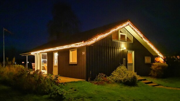 Ein Haus mit geneigtem Dach, der Hausnummer 90 an der Seite und einer Veranda mit einem Stuhl.