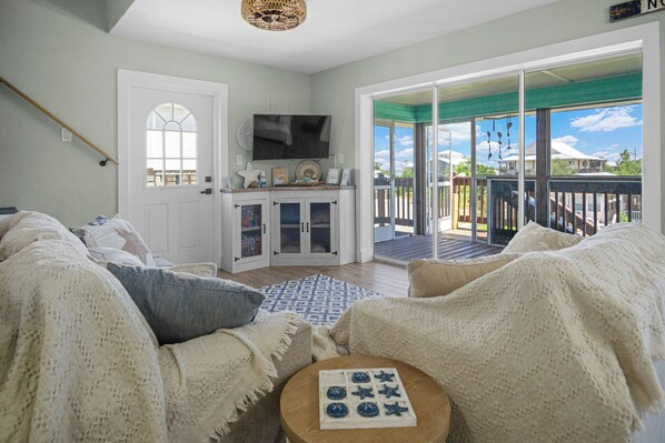 A cozy living room with a large window, a flat-screen TV, and a wooden table with a board game.