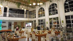 A spacious dining area with multiple tables and chairs, large windows, and hanging plants. - Rocca Del Garda Resort (Cardona)