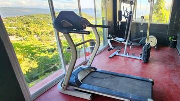 Un gimnasio con cinta de correr, máquinas de pesas y vistas a un paisaje verde a través de amplias ventanas.