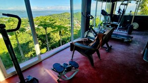 A gym with exercise equipment and a large window offering a view of a green landscape. - Rocca Del Garda Resort (Cardona)