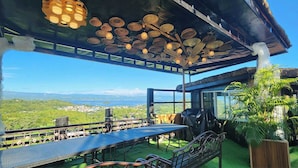 An outdoor dining area with a view of the landscape, a covered seating area with a thatched roof, and a table with chairs. - Rocca Del Garda Resort (Cardona)