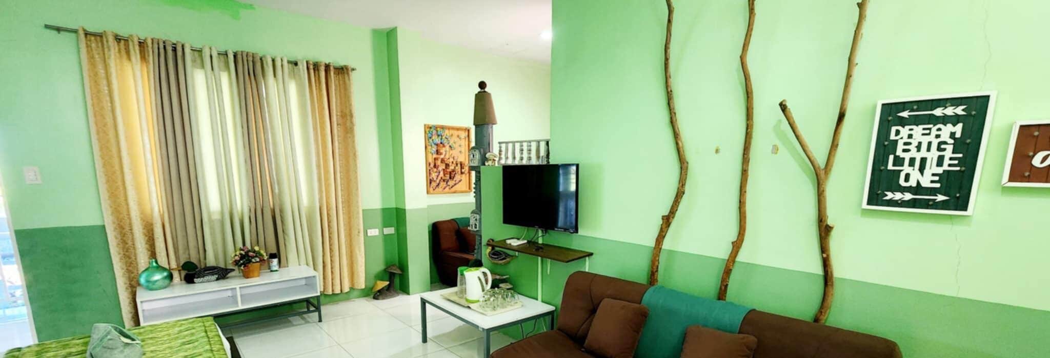 A living room with a sofa, a coffee table, a television, and a wall-mounted TV. There are curtains, a painting, and a branch decoration on the wall.