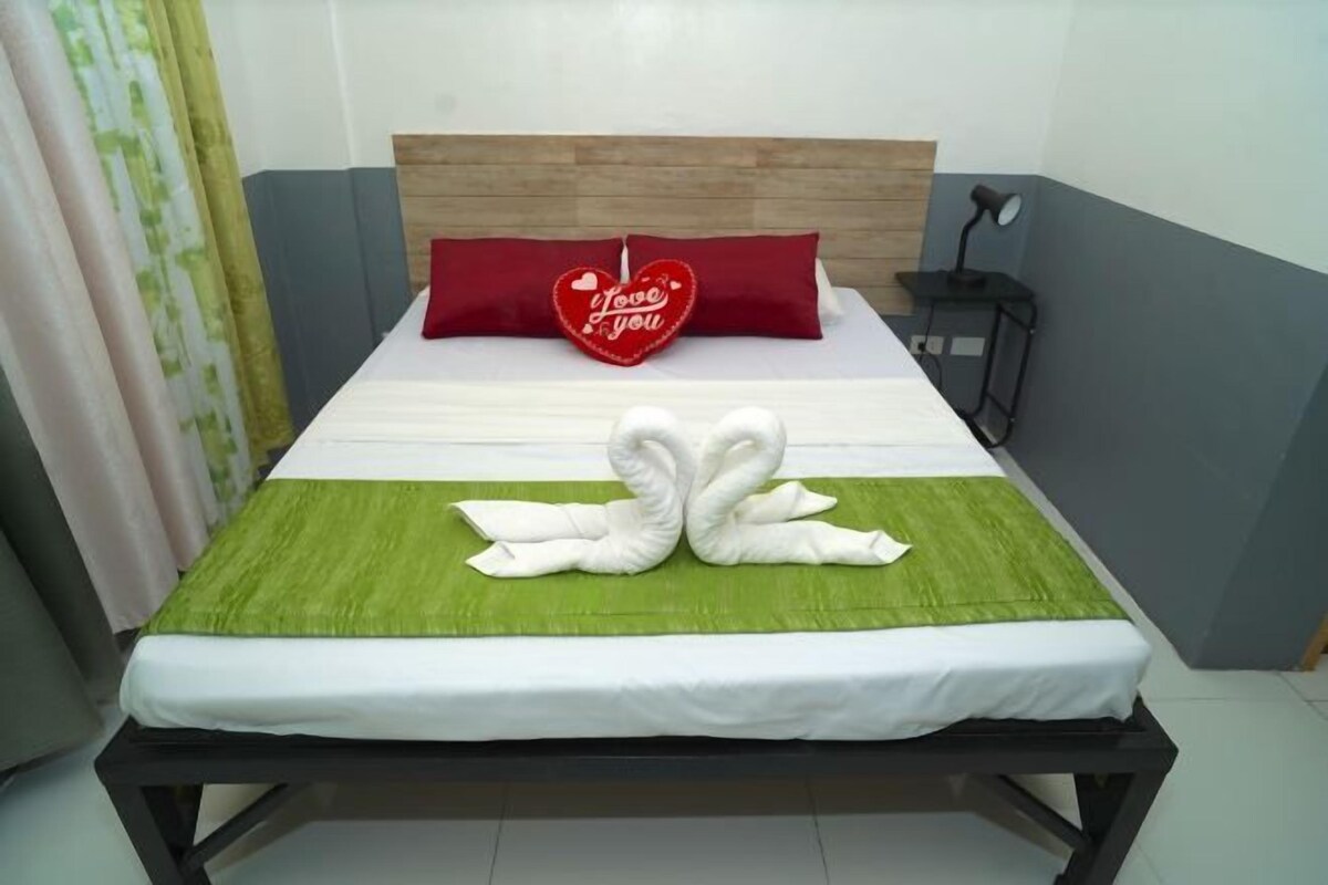 A neatly made bed with a heart-shaped pillow and a swan-shaped towel arrangement.