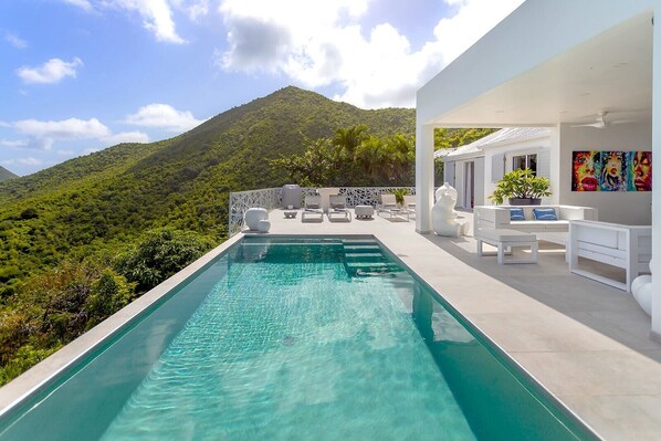 A modern outdoor pool area with a view of a lush green mountain.