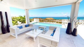 A modern outdoor seating area with white furniture, a pool, and a scenic ocean view.