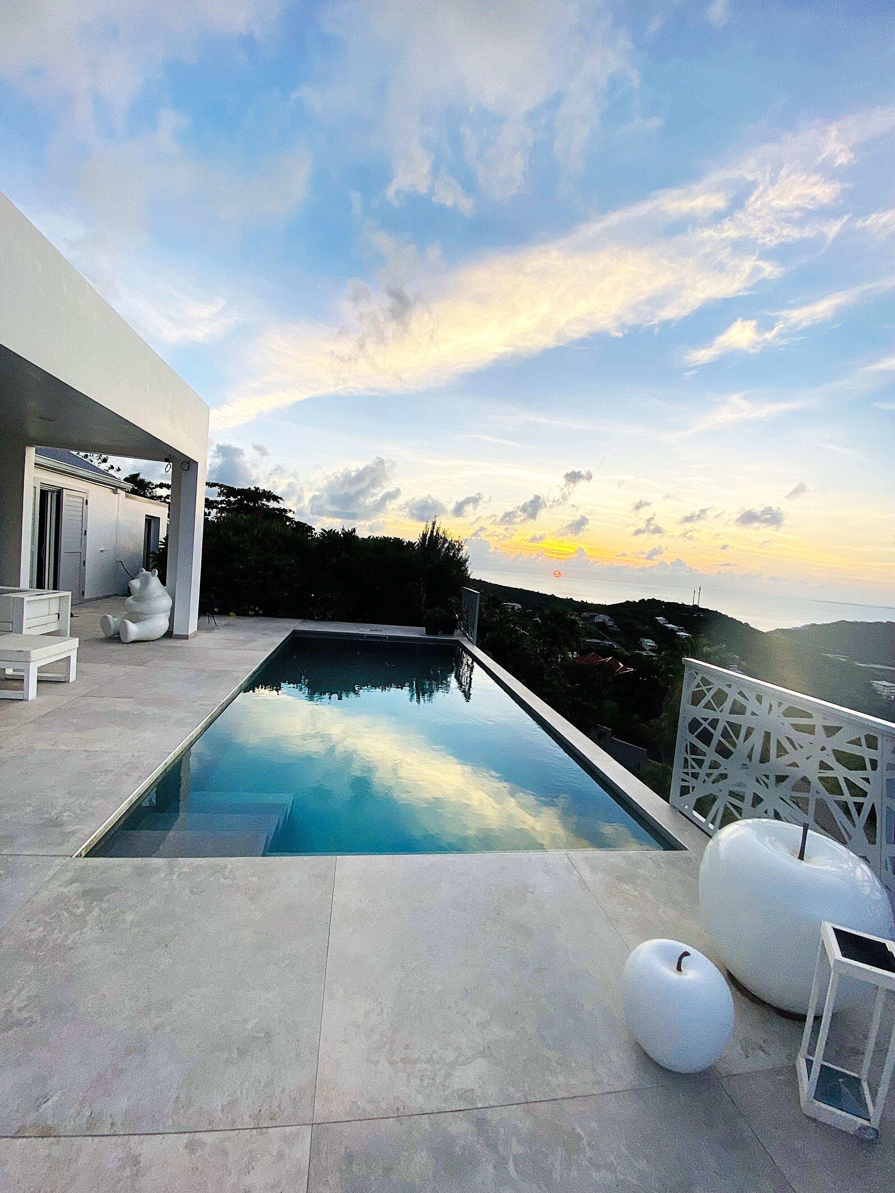 Un espace piscine extérieur moderne offrant une vue dégagée sur le paysage environnant et un coucher de soleil en toile de fond.