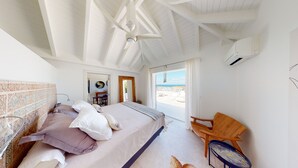 Ein Schlafzimmer mit Bett, Kissen, einem Holzstuhl und Blick auf den Strand.
