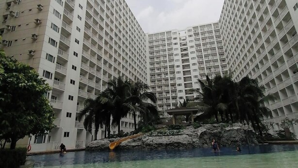 A high-rise residential building with multiple balconies and a pool area with palm trees. - Shawnalyn condotel at Mall of Asia,Philippines (Pasay)