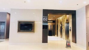 A modern hotel lobby with a flat-screen TV mounted on the wall, a sign indicating the location 'Tower D2', and an elevator in the background. - Shawnalyn condotel at Mall of Asia,Philippines (Pasay)