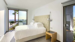 Une chambre moderne avec un grand lit, une petite table de chevet et une vue sur l’extérieur grâce à une porte coulissante.