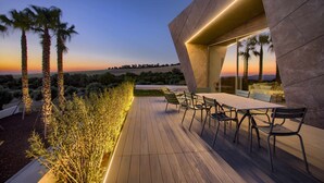 Une terrasse extérieure avec une table et des chaises, des palmiers et un bâtiment moderne doté d’un toit en pente.