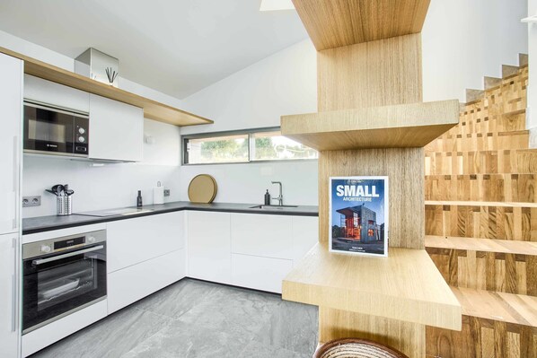 Une cuisine moderne avec des meubles blancs, un four Bosch et un escalier en bois.