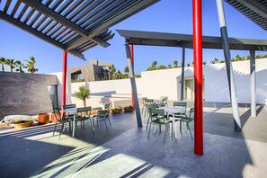 Un espace extérieur aménagé en terrasse, avec une pergola, des piliers rouges et des chaises vertes.