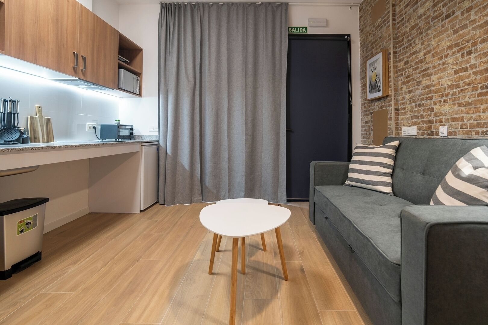 A modern kitchen with wooden cabinets, a grey sofa, and a white table.