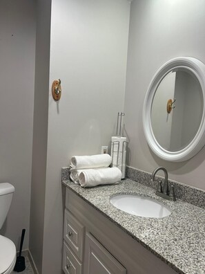 Un bagno con un piano in granito, un lavandino bianco, uno specchio rotondo e due asciugamani sul ripiano.