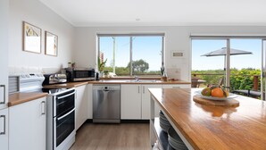 Une cuisine moderne avec des armoires blanches, des appareils en acier inoxydable et un comptoir en bois. Une grande fenêtre offre une vue sur l’extérieur.