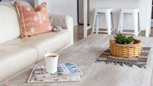 Un salon avec un canapé blanc, une table basse sur laquelle se trouve un magazine, une tasse de café et un panier en osier contenant une plante.