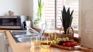 Un comptoir de cuisine avec une carafe de thé, trois verres, un panier de raisins et une plante en pot.