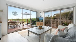 Un vaste espace de vie avec une grande porte-fenêtre coulissante donnant sur une terrasse extérieure, une table basse en bois et un canapé confortable.