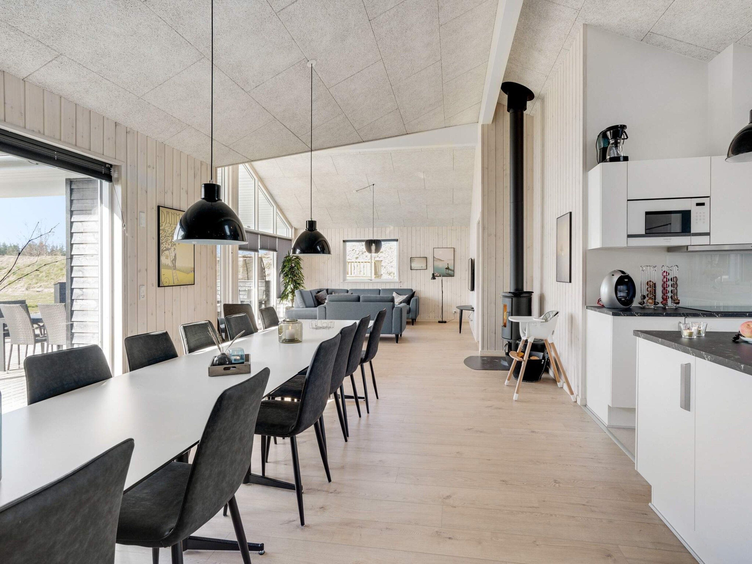 A modern kitchen with a long dining table, a built-in stove, and white cabinetry.