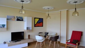 A modern living room with a flat-screen TV, a dining table with chairs, and a red armchair. - Cozy apartment with views in Sada (Sada)