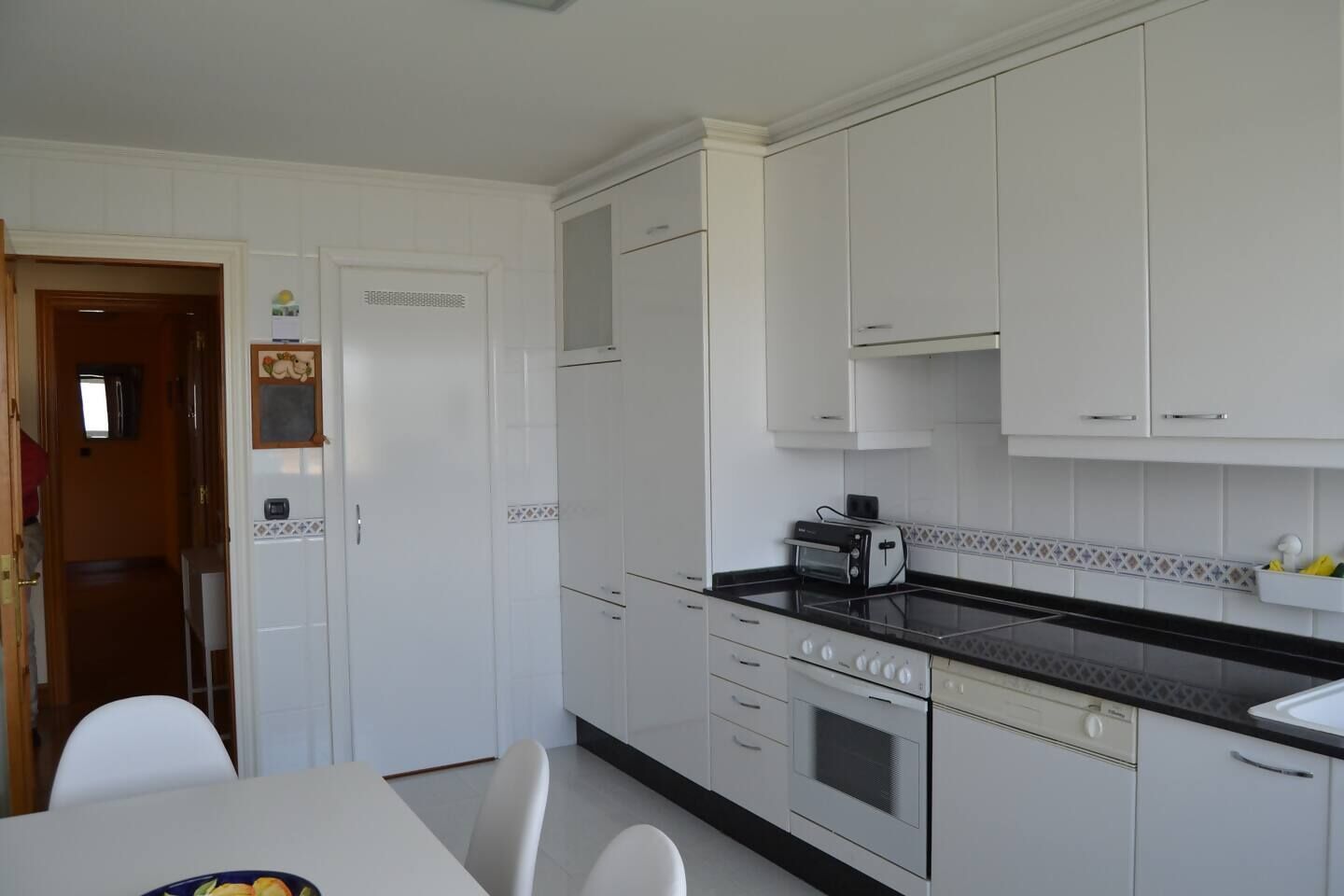 A compact kitchen with white cabinets, a black countertop, a toaster, and a dining area with a table and chairs.