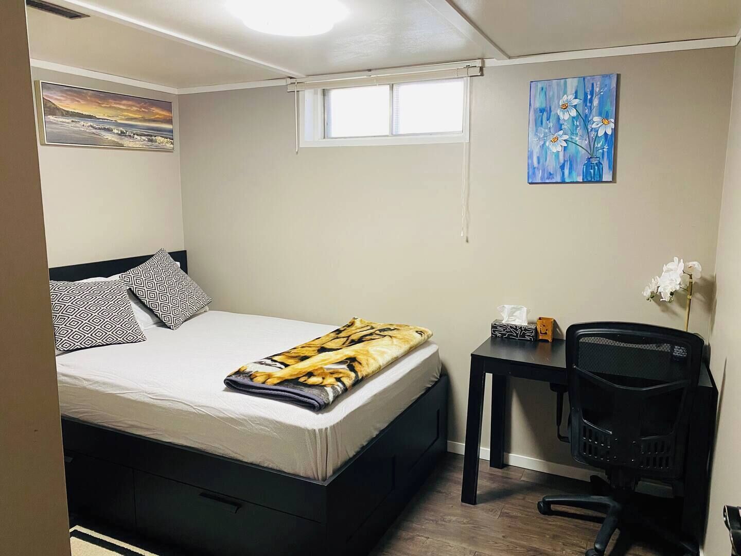 A compact bedroom with a bed, a desk, and a chair. There are two paintings on the walls.