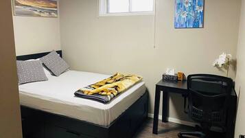 A compact bedroom with a bed, a desk, and a chair. There are two paintings on the walls.