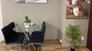 Un coin repas avec une table en verre, deux chaises noires, une plante en pot et deux œuvres d’art accrochées aux murs.