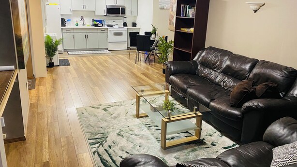 Un salon avec un canapé en cuir, une table basse en verre et une cuisine à l’arrière-plan.
