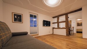 Un salon moderne avec un canapé gris, un plancher en bois, un téléviseur fixé au mur et un coin repas comprenant une table et des chaises en bois.
