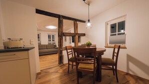 Un coin repas avec une table et des chaises en bois, un luminaire suspendu et une fenêtre avec des stores.