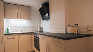 Une cuisine moderne avec des armoires de couleur beige, un plan de travail noir et un four encastré.