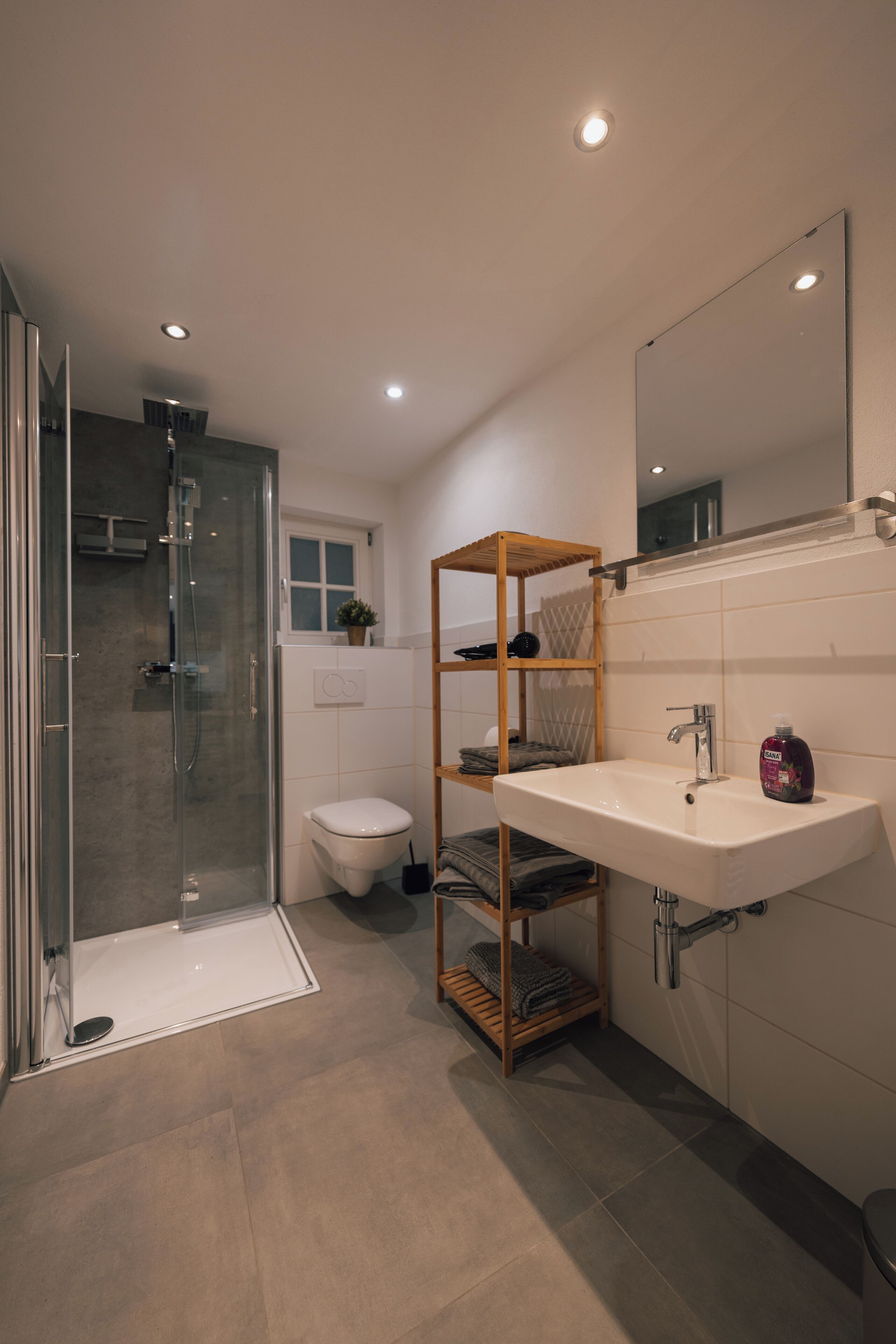 Une salle de bain moderne avec une douche à parois de verre, un lavabo blanc et une étagère en bois.