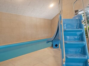 A blue pool with a slide, beige tiled walls, and a metal handrail. - 5 Star Holiday Home in Aakirkeby (Akirkeby)