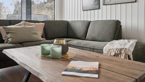Una sala de estar moderna con un sofá seccional gris, una mesa de centro de madera con velas y un libro, y dos obras de arte enmarcadas en la pared.