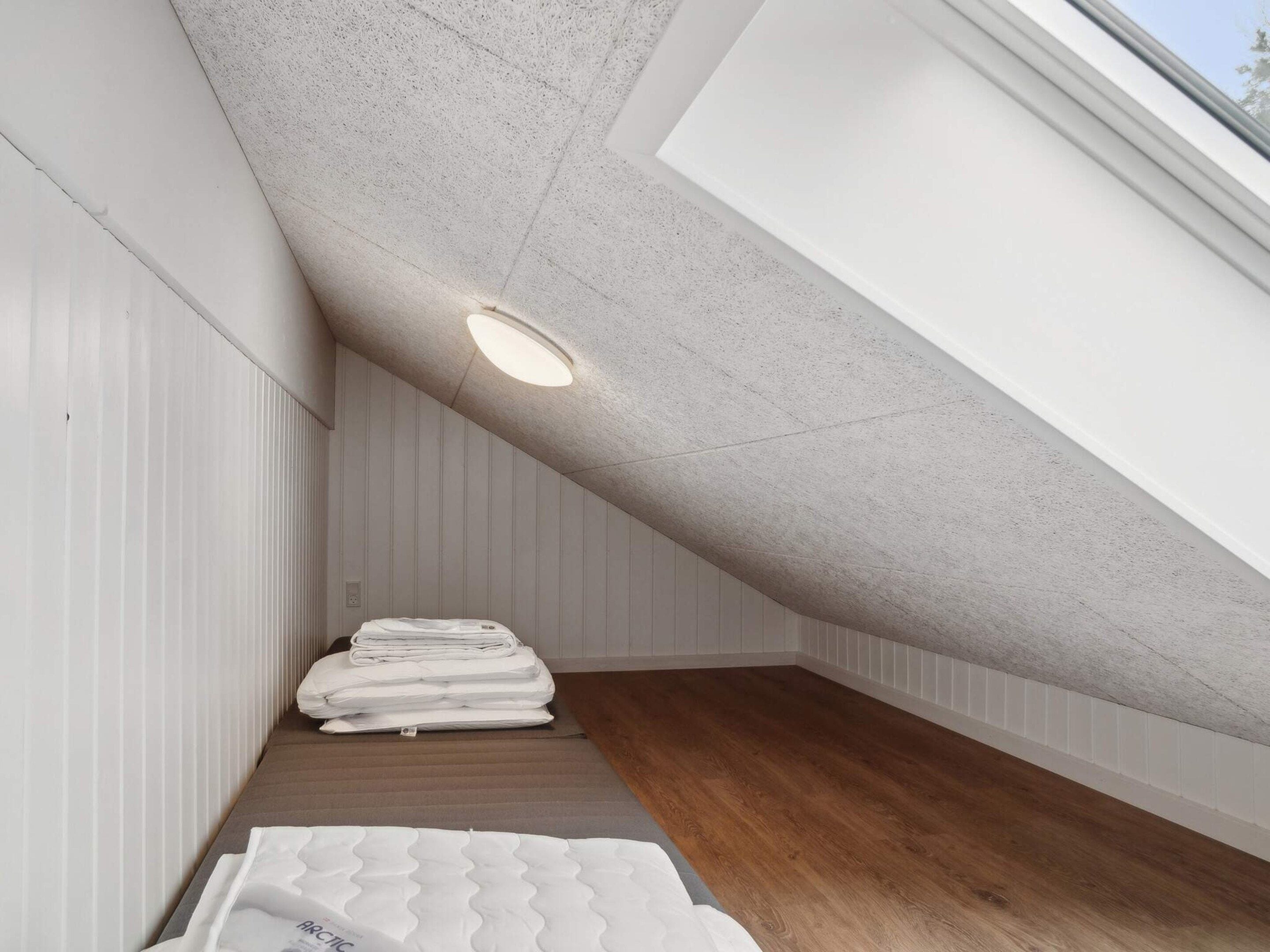 A room with sloped ceilings, a skylight, and a stack of mattresses.