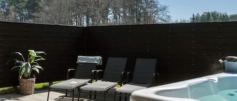 A patio area with a hot tub, lounge chairs, and a potted plant.