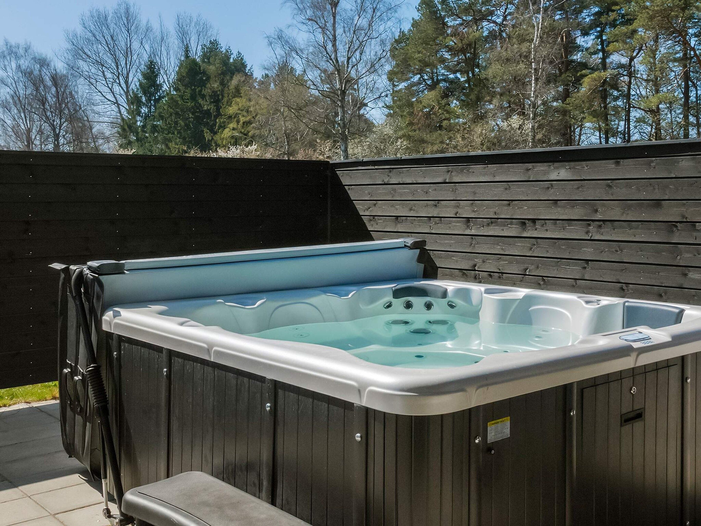 A rectangular hot tub with a built-in seat, surrounded by a wooden deck, set against a backdrop of trees.
