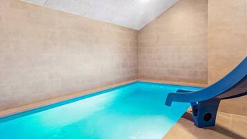 Une piscine avec un toboggan bleu, des murs recouverts de carreaux beiges et un plafond doté d’un éclairage encastré.