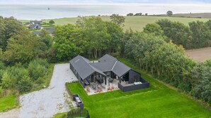 A modern house with a large patio, surrounded by lush greenery and a view of the sea. - 5 Star Holiday Home in Sydals (Sydals)