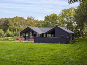 A modern two-story house with a dark exterior, large windows, and a covered outdoor seating area.