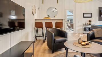A modern living room with a flat-screen TV, leather sofas, a round coffee table, and a dining area with bar stools.