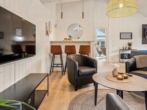 A modern living room with a flat-screen TV, leather sofas, a round coffee table, and a dining area with bar stools.